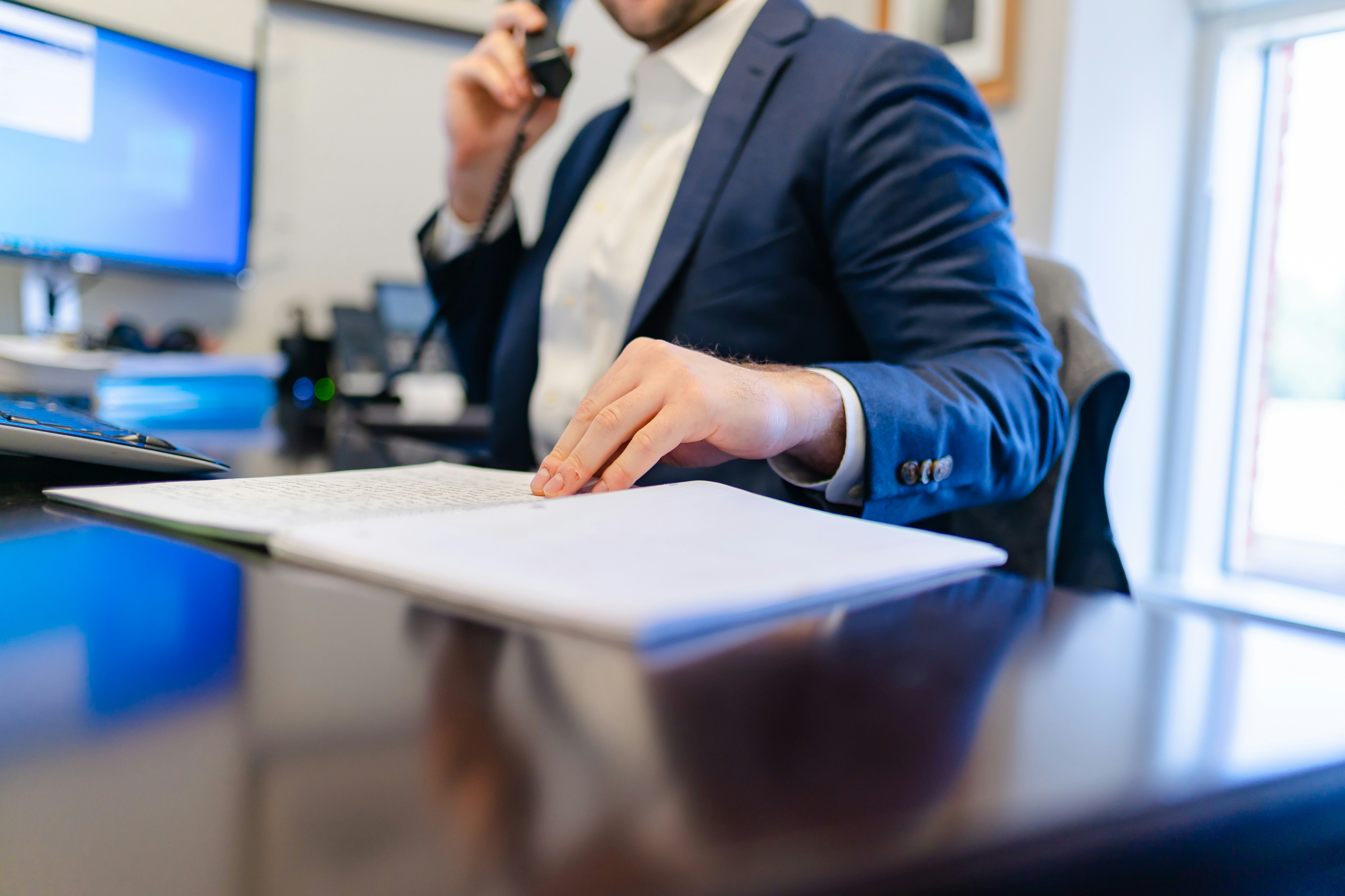 Serious millennial man using laptop sitting at the table in a home office, focused guy in casual clothing looking at the paper, communicating online, writing emails, distantly working or studying on computer at home.